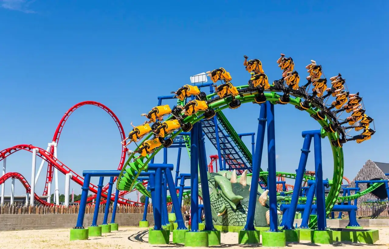 Kolejka górska Hyperion z żółtymi wagonikami na zielonym torze, w tle czerwona kolejka.