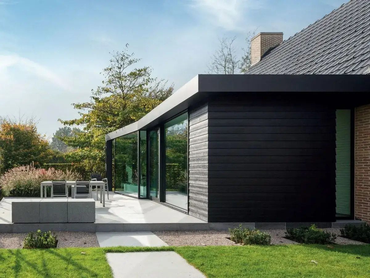 Nowoczesny dom z czarną elewacją drewnianą i dużymi oknami, otoczony ogrodem.