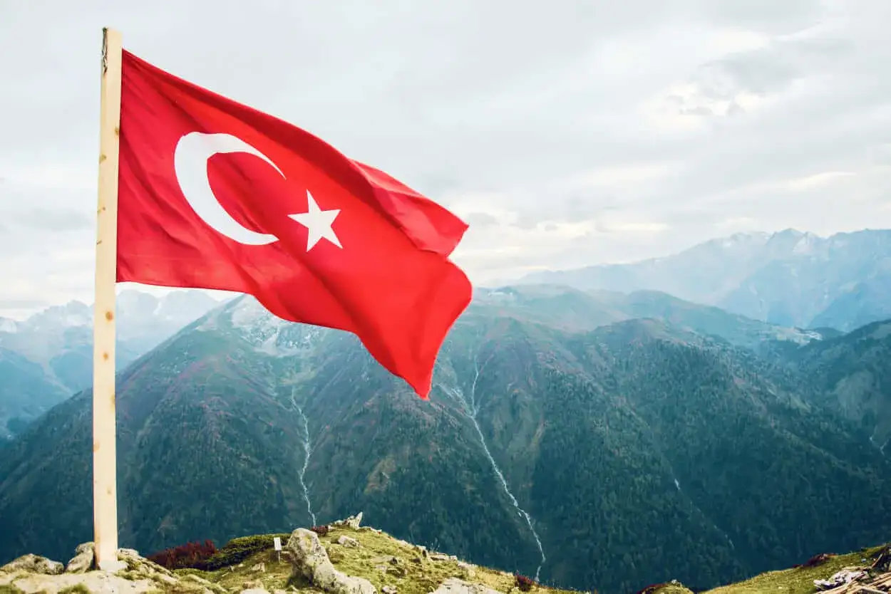 Turecka flaga powiewa na tle górskich krajobrazów. Zastanawiasz się, ile trwa lot do Turcji?