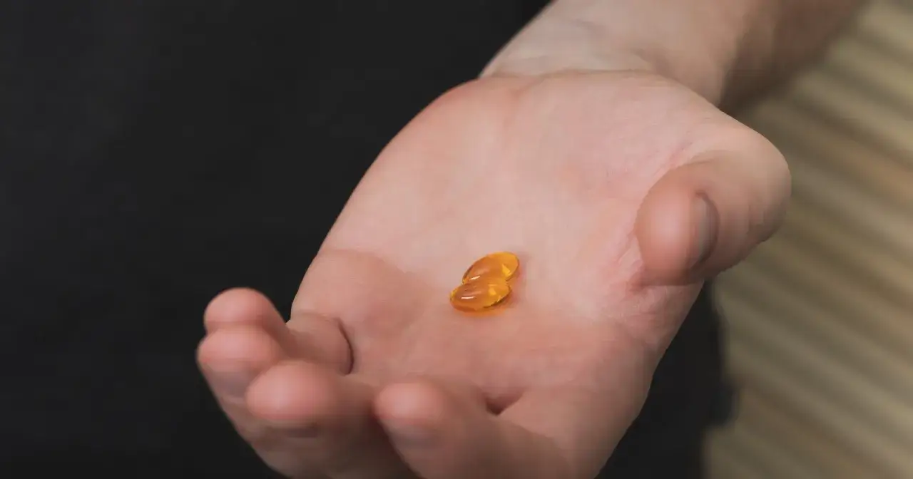 Dwie bursztynowe kapsułki na dłoni, symbolizujące walkę z niedoborem witaminy D3.