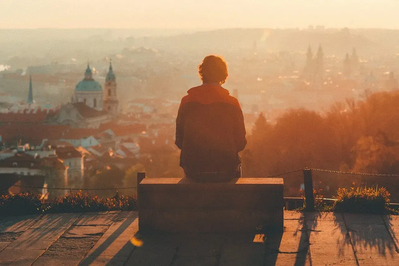 Osoba siedzi na ławce, patrząc na miasto w zachodzącym słońcu. Może to być moment refleksji nad zespołem pomijania stronnego.
