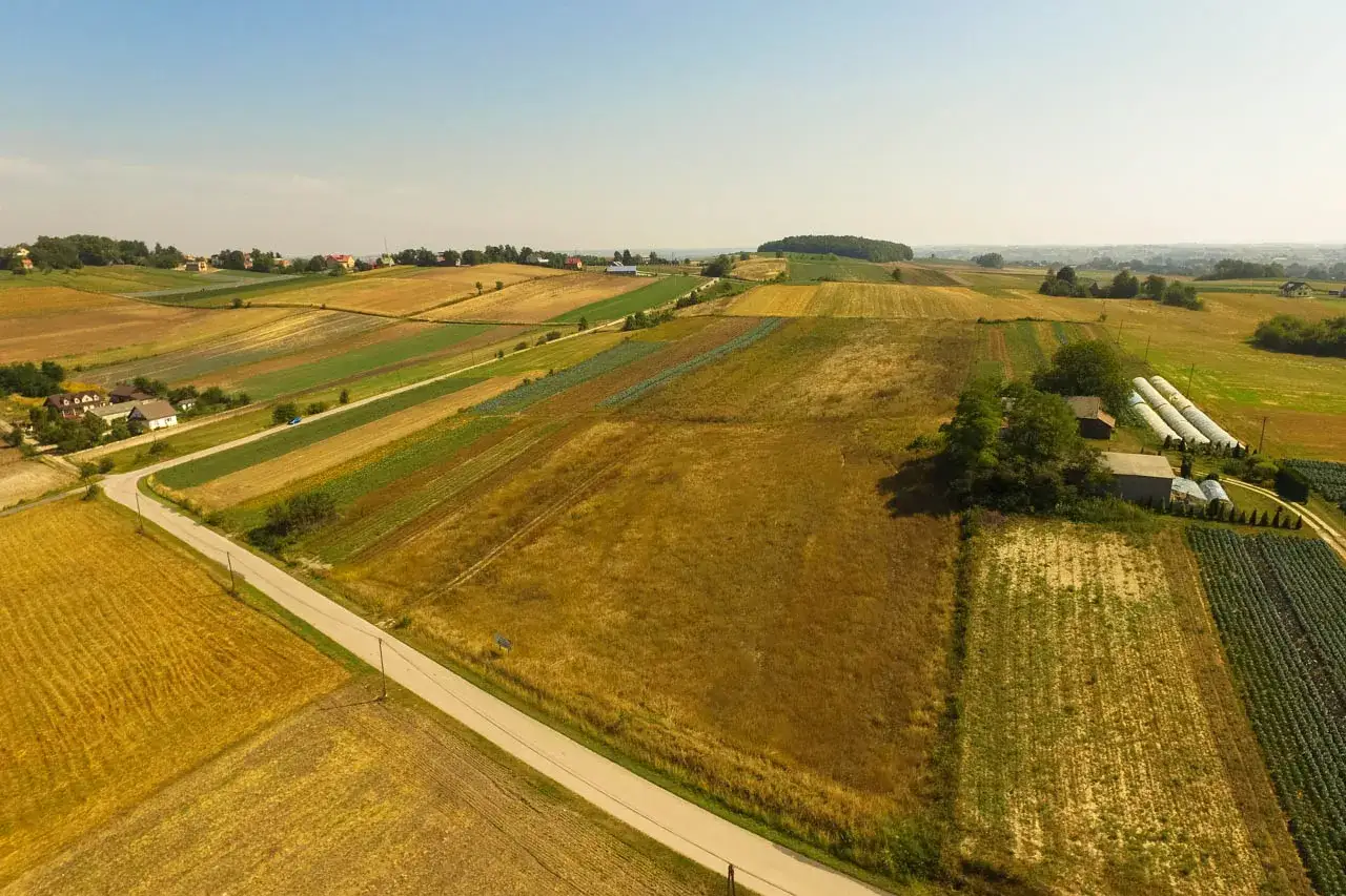 Widok z lotu ptaka na patchwork pól uprawnych, domy i szklarnie. Kto płaci podatek od dzierżawy gruntu? Rolnicy, którzy uprawiają te ziemie.