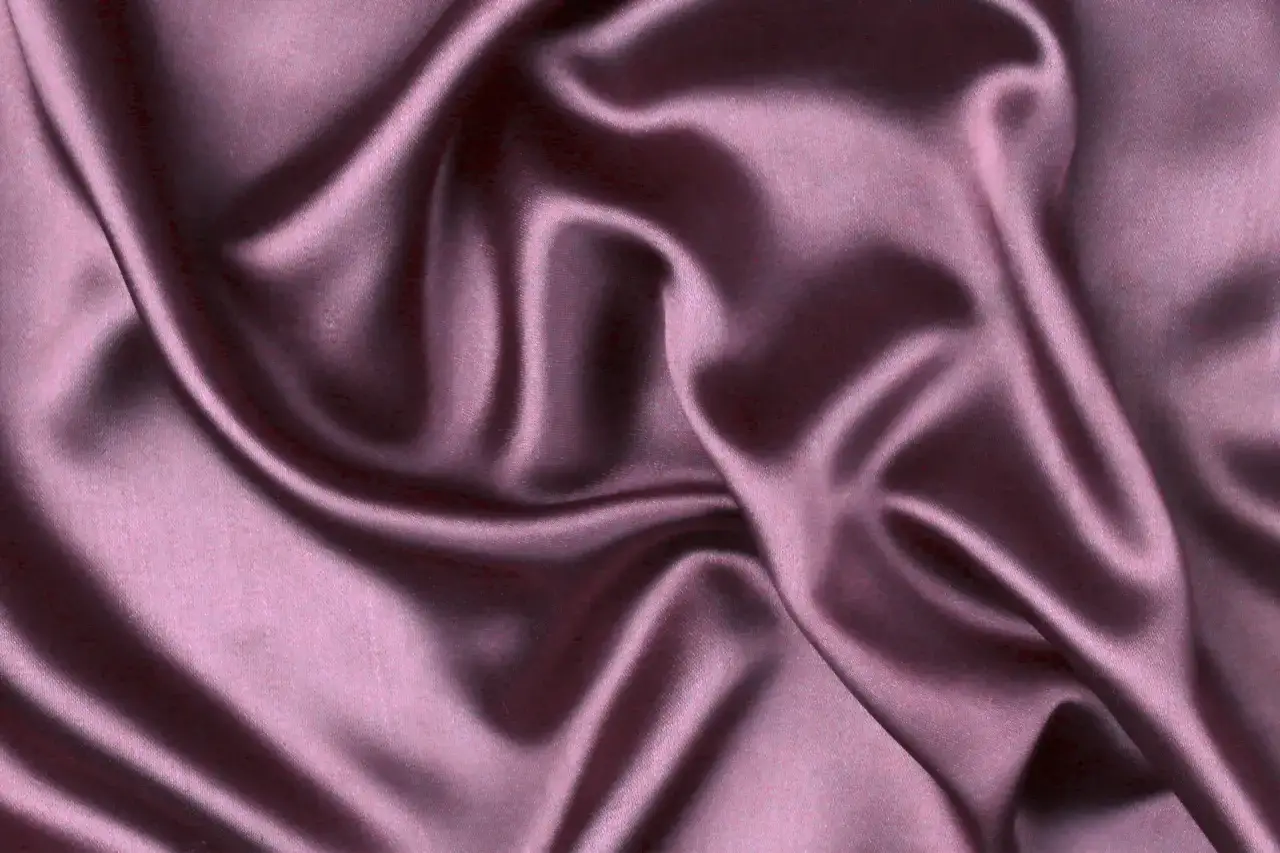 Gładka, błyszcząca satyna w kolorze pudrowego różu, układająca się w miękkie fale. To właśnie satyna, co to za materiał?