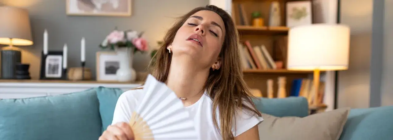 Kobieta z zamkniętymi oczami wachluje się wachlarzem, odczuwając uderzenia gorąca.