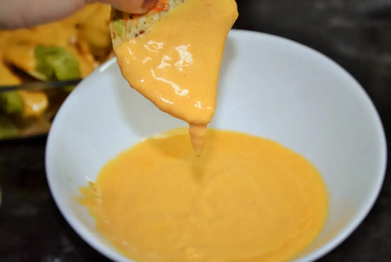 Un totopo cubierto de queso fundido cremoso se sumerge en un tazón de queso.