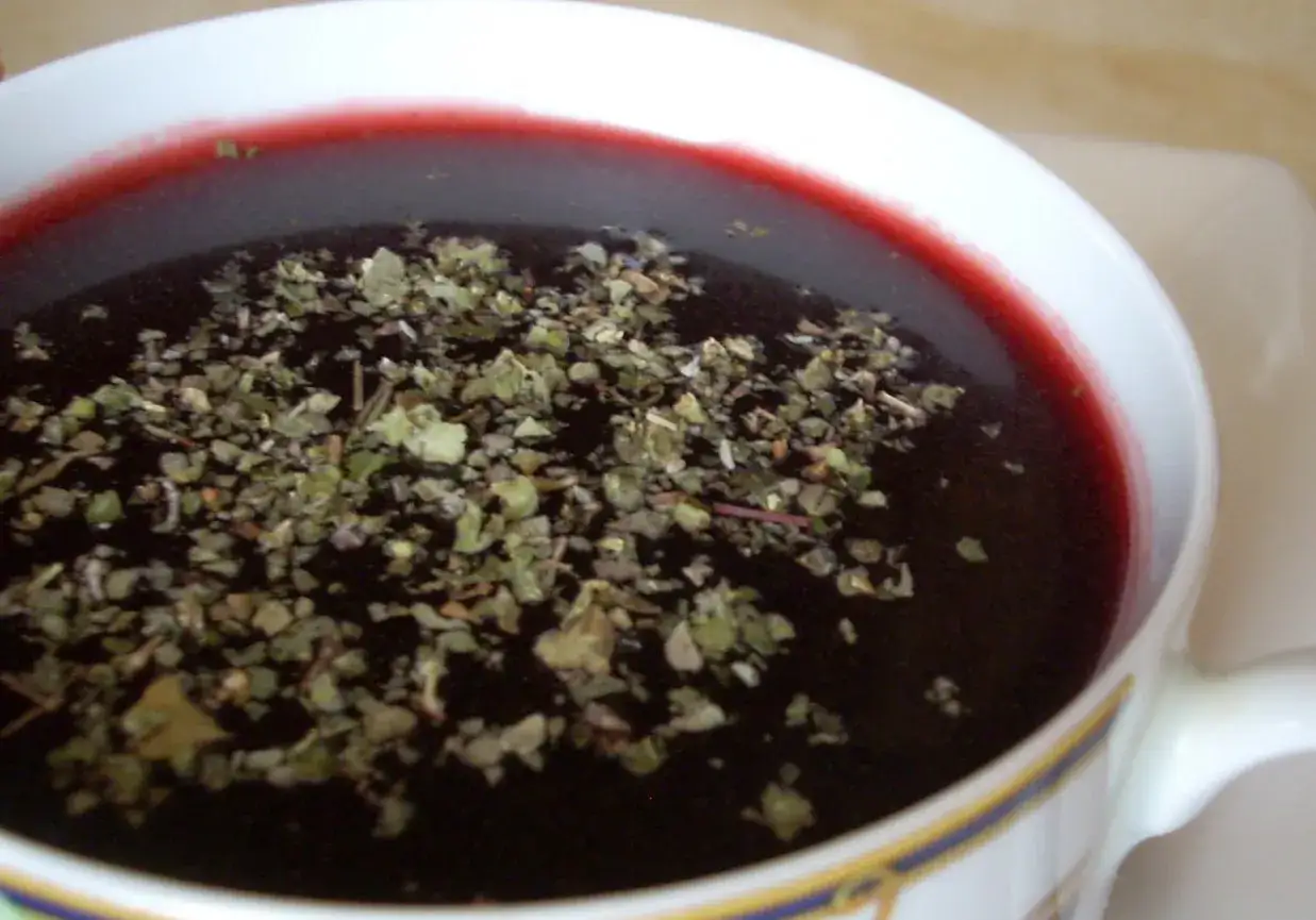 Czy do barszczu czerwonego dodaje się majeranek? Widać go na powierzchni tej głębokiej, rubinowej zupy w białej filiżance.