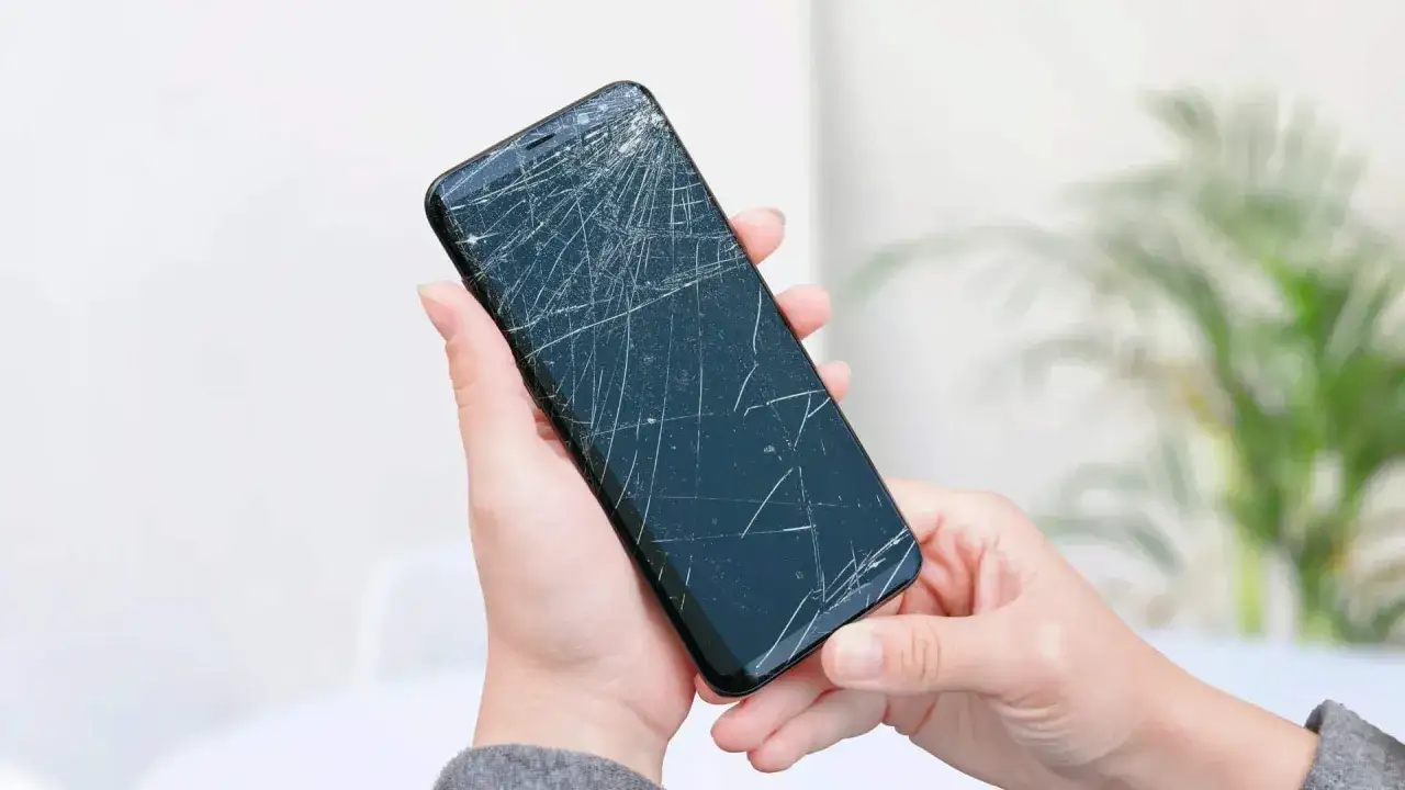 Dwie dłonie trzymają pęknięty telefon, czekając na wymianę dotyku.