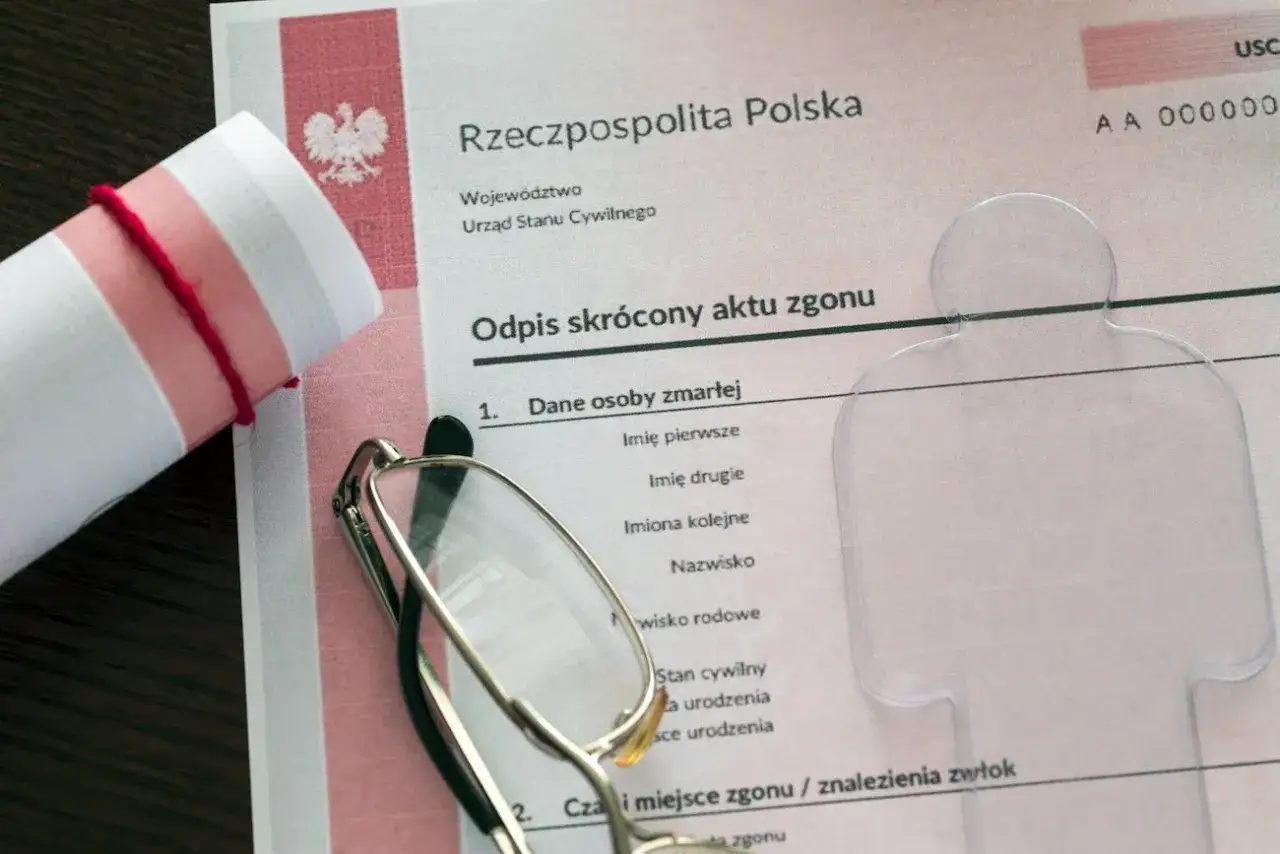 Odpis skrócony aktu zgonu z okularami i zrolowanym dokumentem.
