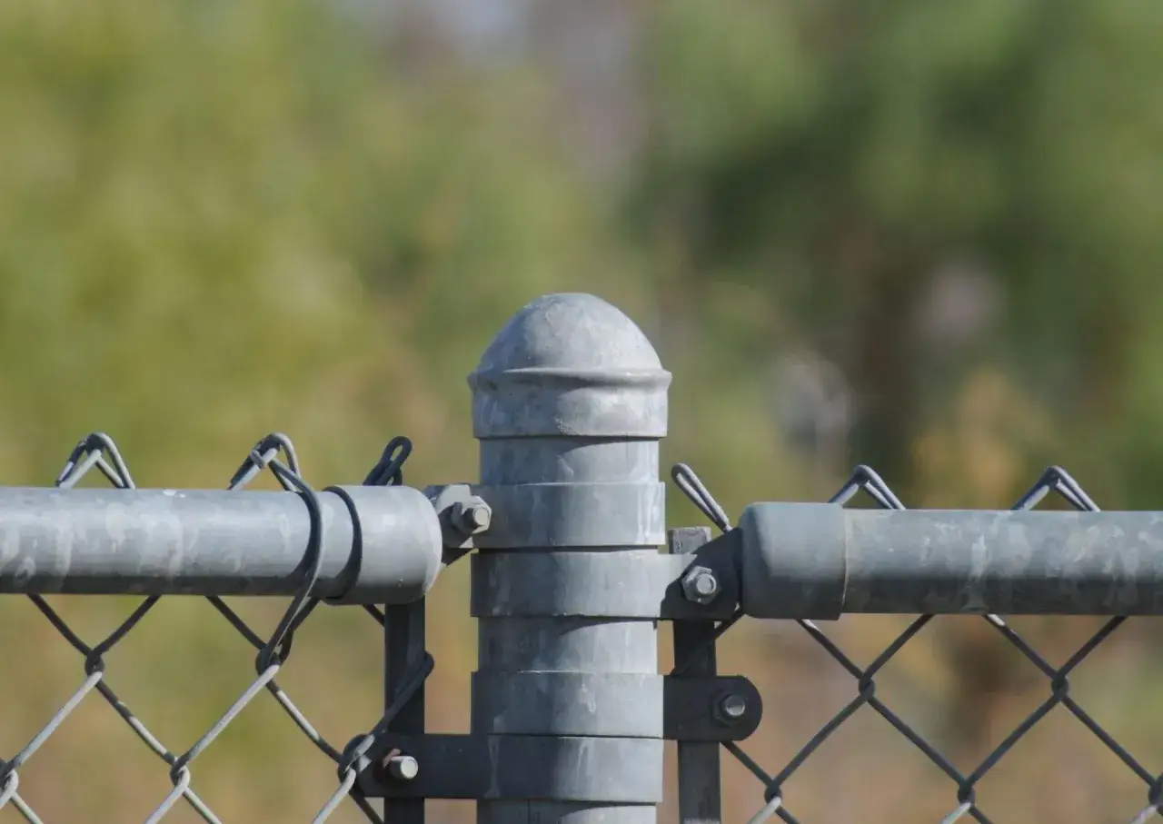 Szczegółowy montaż słupków ogrodzeniowych instrukcja: zbliżenie na metalowy słup z siatką i rurą.