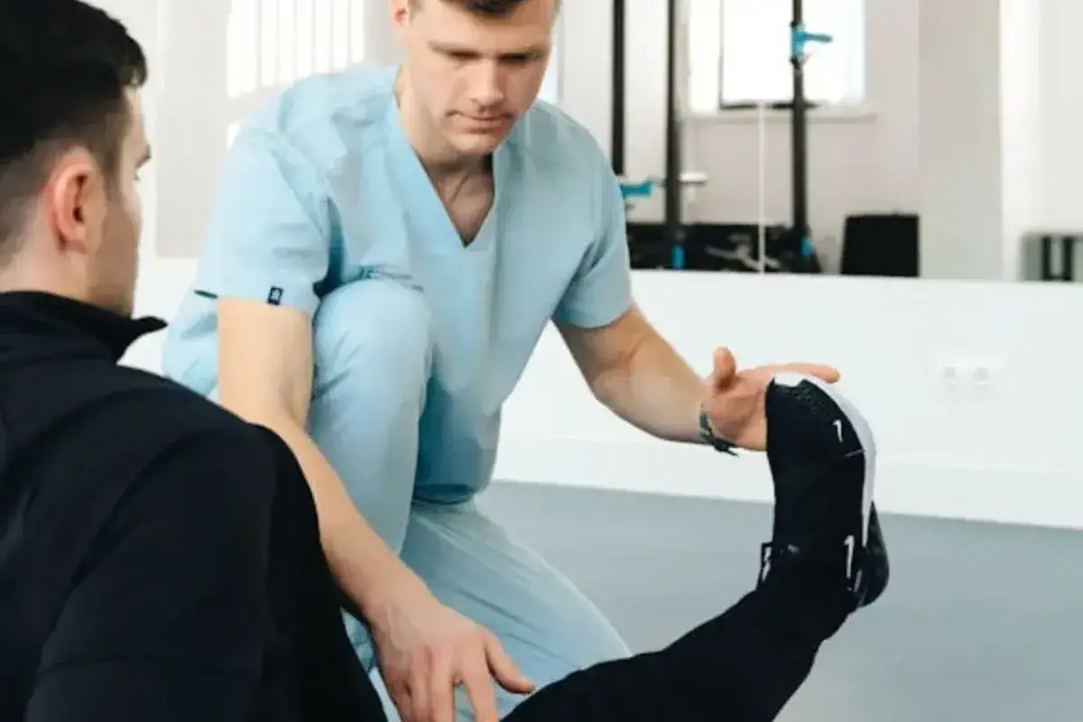 Fizjoterapeuta w jasnoniebieskim uniformie pomaga pacjentowi w ćwiczeniach rehabilitacyjnych.