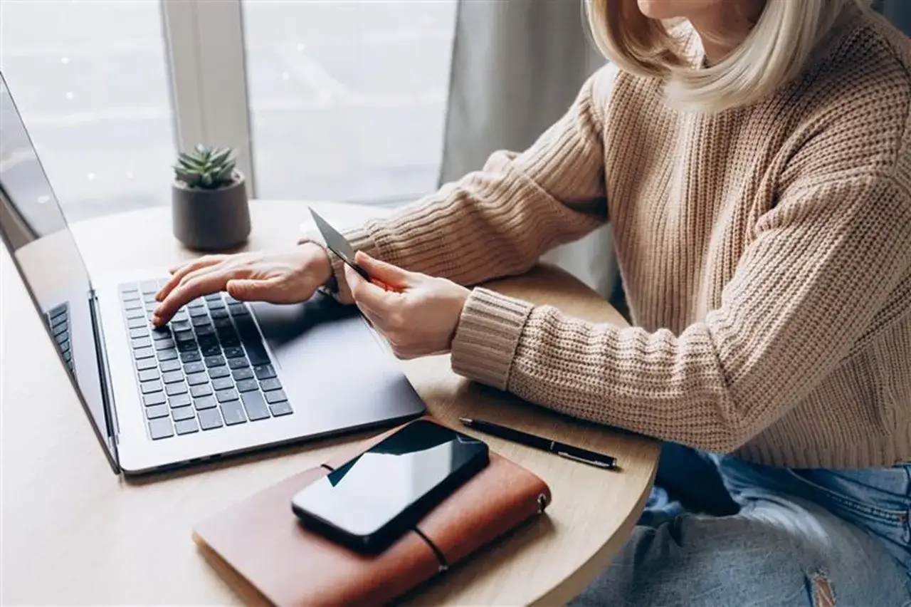 Kobieta z kartą płatniczą przy laptopie, szuka informacji, jak sprawdzić numer karty w aplikacji IKO.