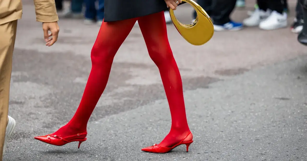 Kobieta w czerwonych rajstopach i czerwonych butach na obcasie, z żółtą torebką. Stylowe czerwone buty dodają charakteru damskim stylizacjom.