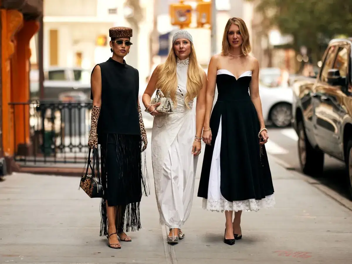 Trzy kobiety prezentują stylowe sukienki maxi. Jedna w czerni z frędzlami i panterką, druga w bieli, trzecia w czarno-białej kreacji.