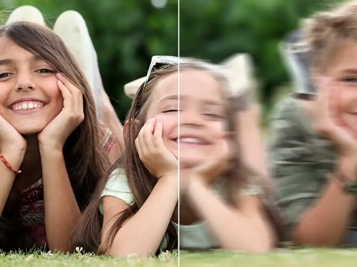 Dwie dziewczynki leżące na trawie, jedna wyraźna, druga rozmazana.