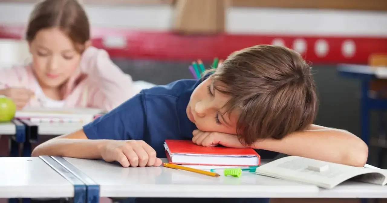 Chłopiec śpi na książce w szkole. Może to być jeden z powodów usprawiedliwienia nieobecności w szkole, gdy brakuje mu sił na naukę.