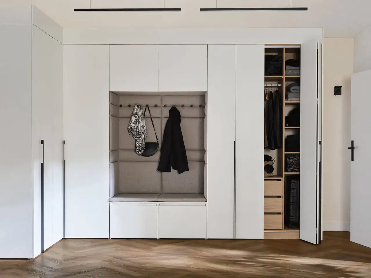 Nowoczesna zabudowa wnęki w przedpokoju z tapicerowanym siedziskiem i otwartą szafą.