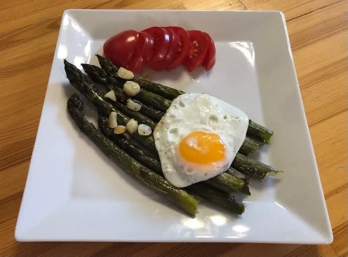 Szparagi z jajkiem sadzonym i pomidorem na białym talerzu.