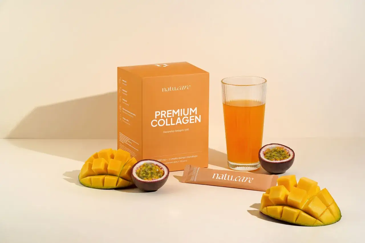 Pudełko z napisem "PREMIUM COLLAGEN Naturalny kolagen rybi", szklanka z pomarańczowym napojem, kawałki mango i marakui.