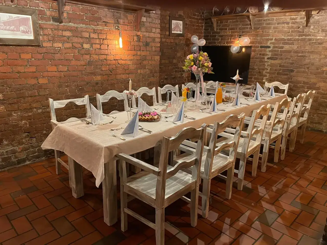 Ustawiony stół w restauracji z białymi obrusami, serwetkami, kwiatami i balonami.