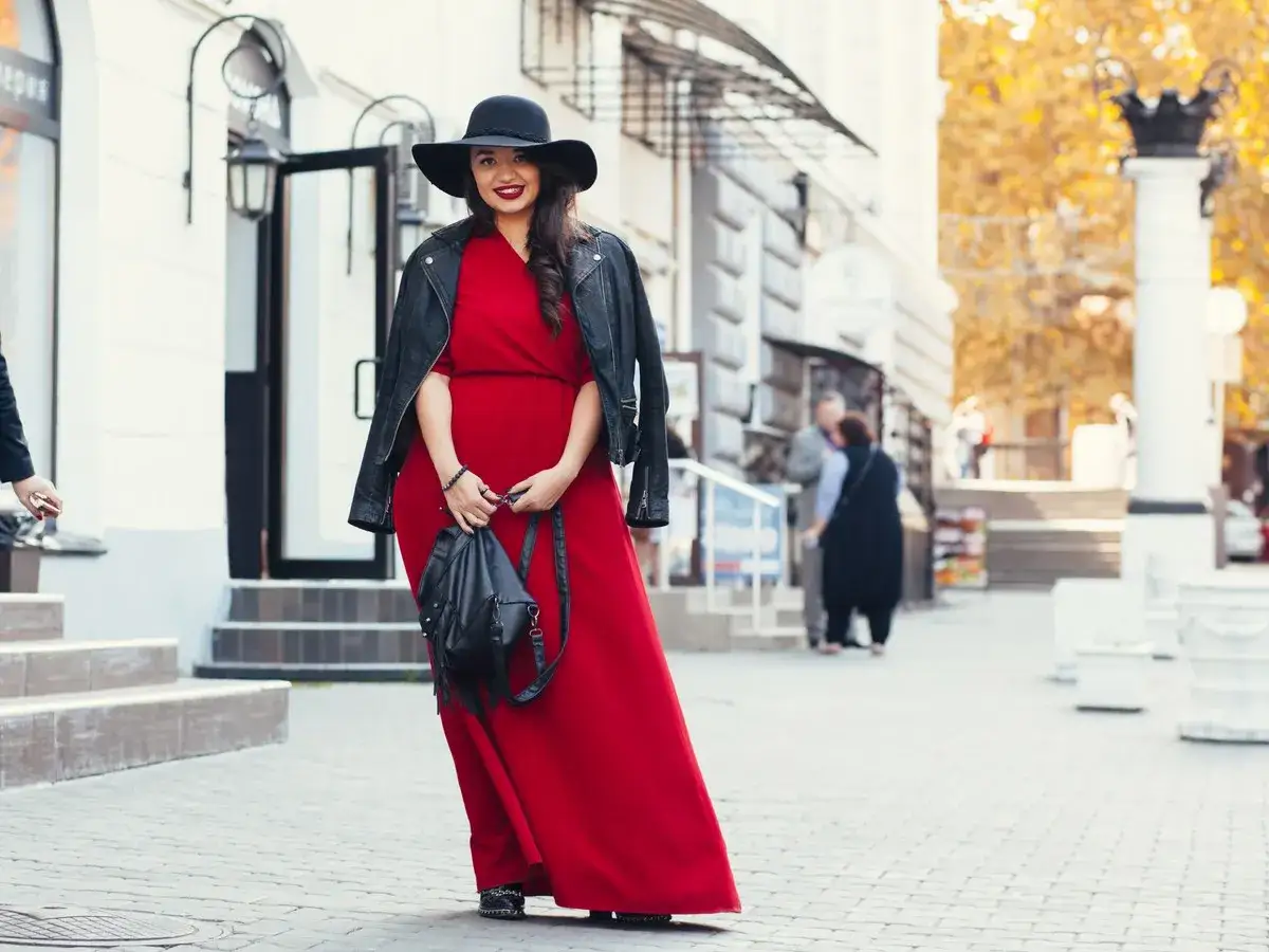 Kobieta w czerwonej sukni i czarnej ramonesce prezentuje stylowe stylizacje dla grubych nóg. Czarny kapelusz dodaje elegancji.