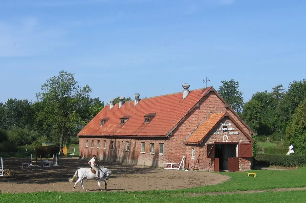 Jazda konna na tle ceglanej stajni z czerwonym dachem.
