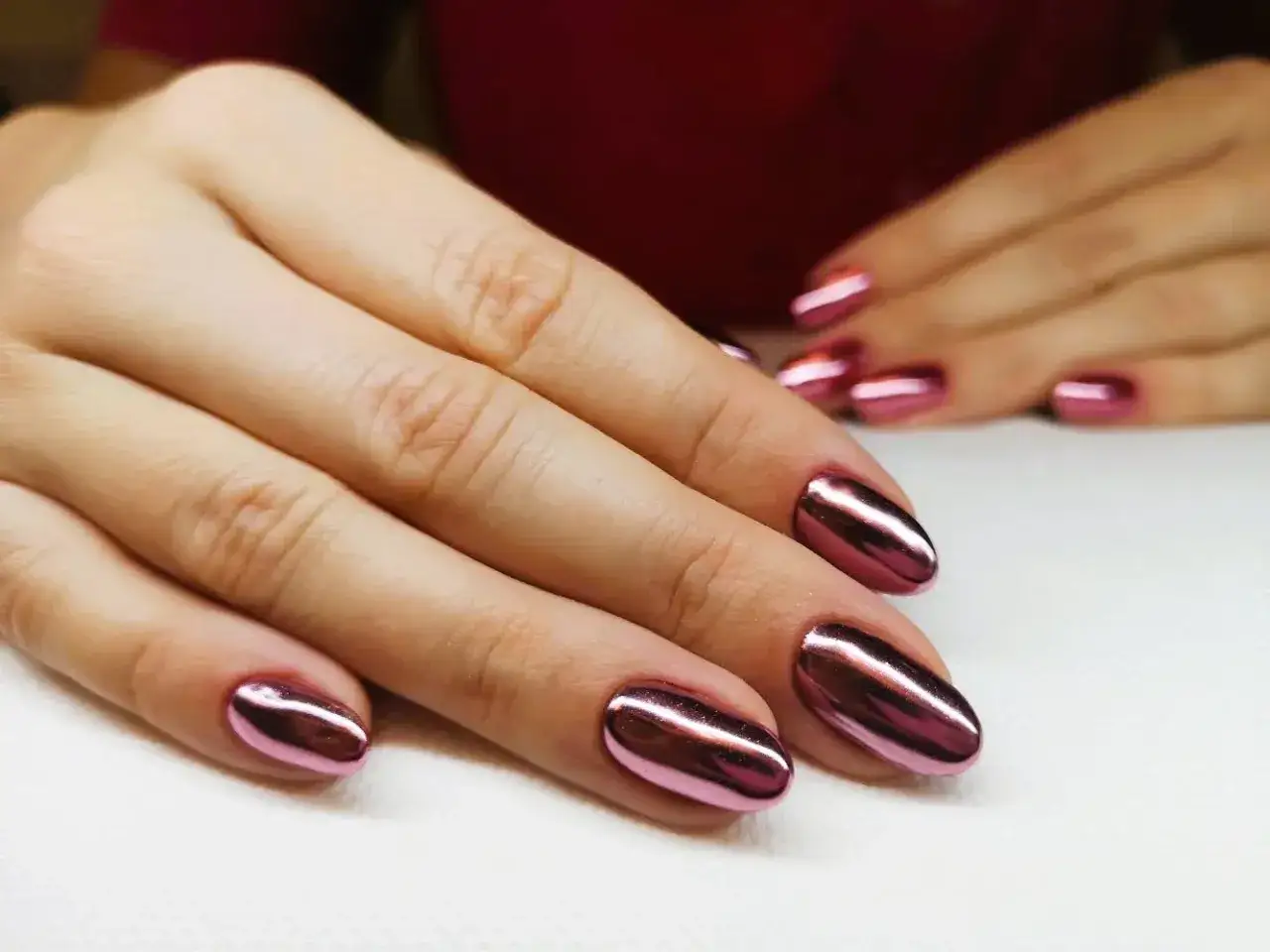 Dłonie z błyszczącym, metalicznym różowym manicure tytanowym. Czy ten efektowny manicure tytanowy rakotwórczy jest wart ryzyka?