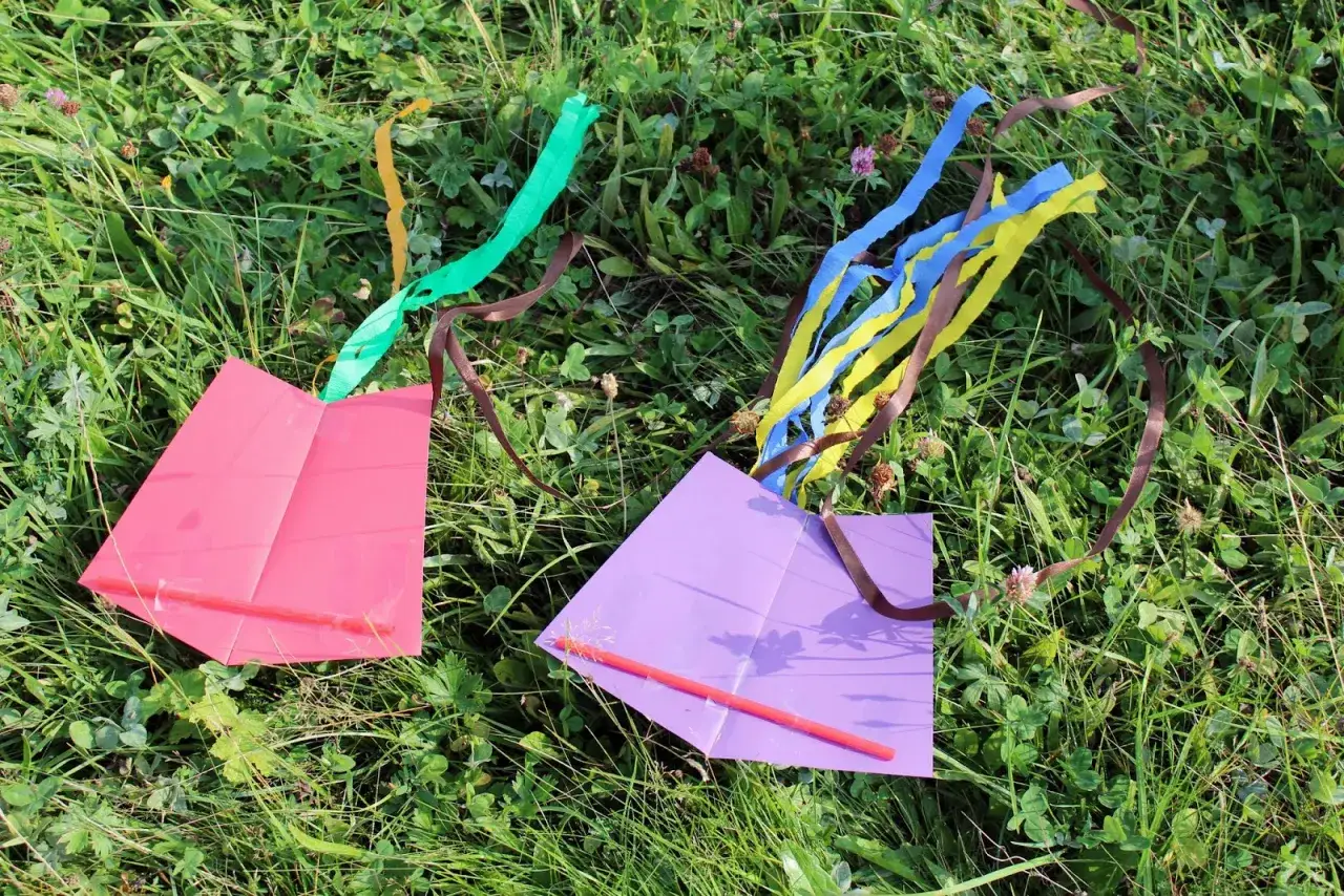 Dwa proste latawce, różowy i fioletowy, leżą na trawie. Idealne, by pokazać jak zrobić latawiec.