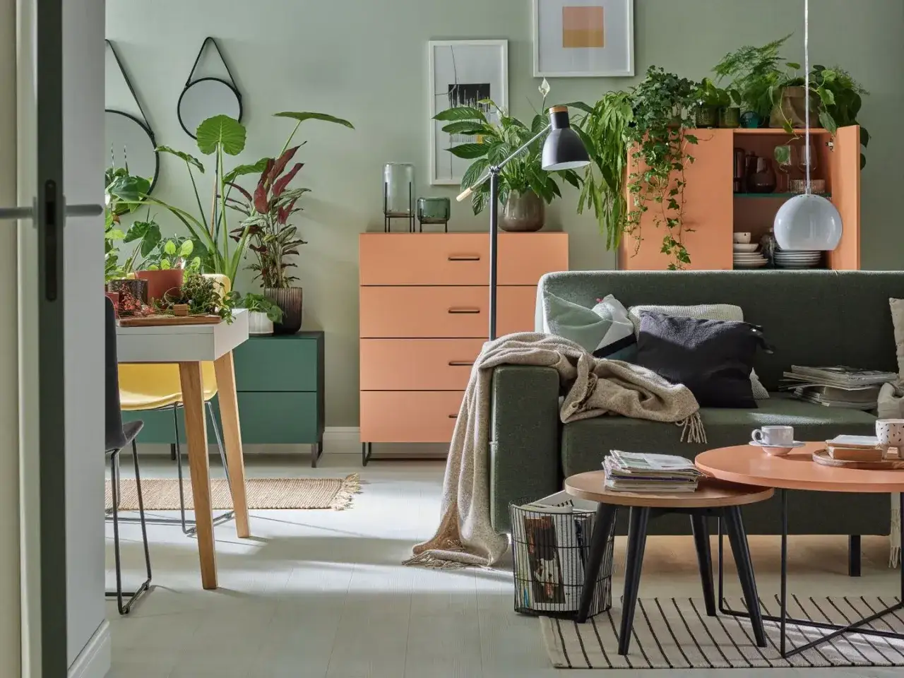 Salon z kanapą w kolorze zielonym i meblami w odcieniach pomarańczowego. Mnóstwo roślin tworzy przytulną atmosferę.