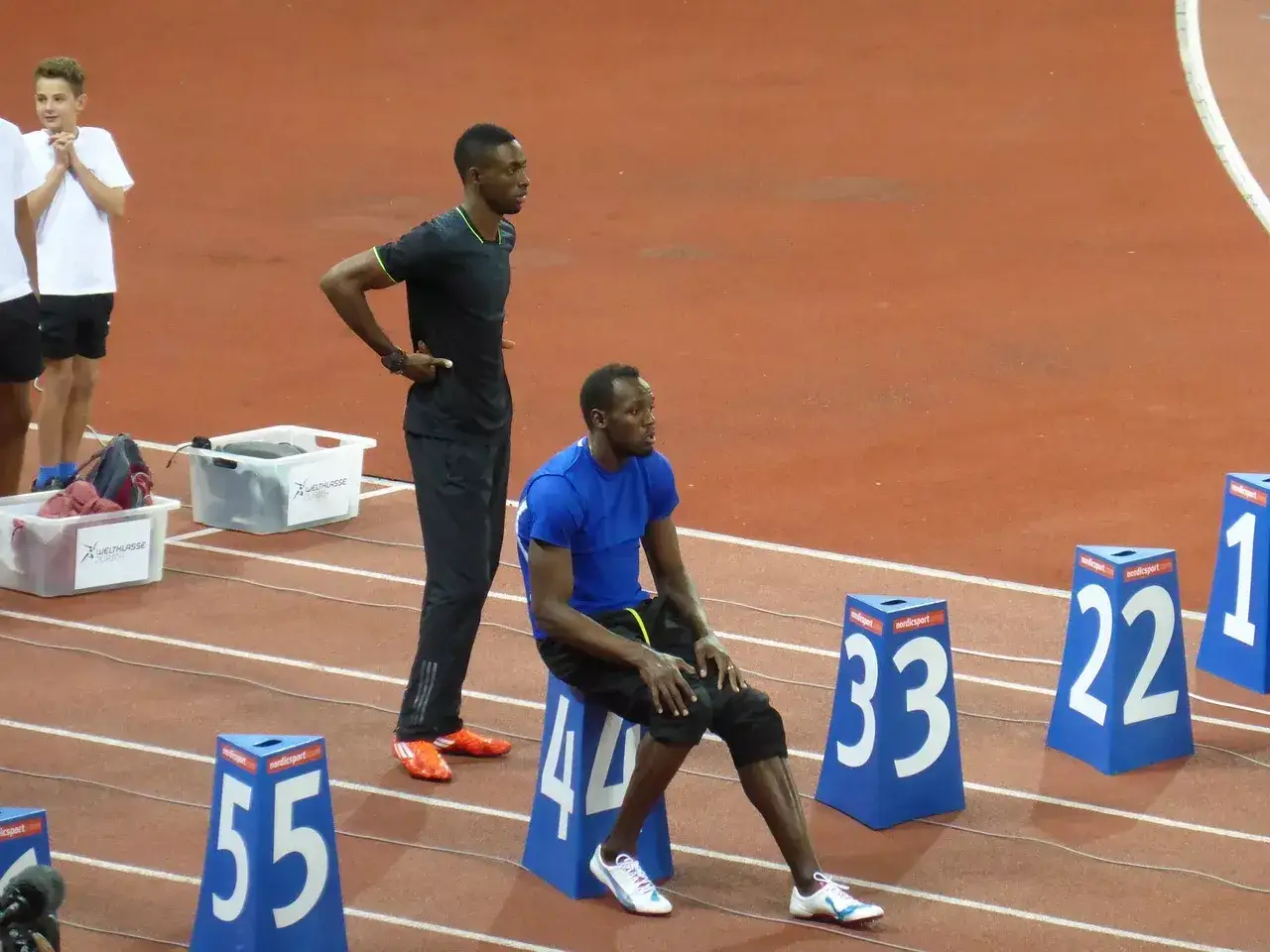Usain Bolt, siedzący i stojący na bieżni, przypomina o jego rekordowej prędkości, która osiągnęła ponad 44 km/h.