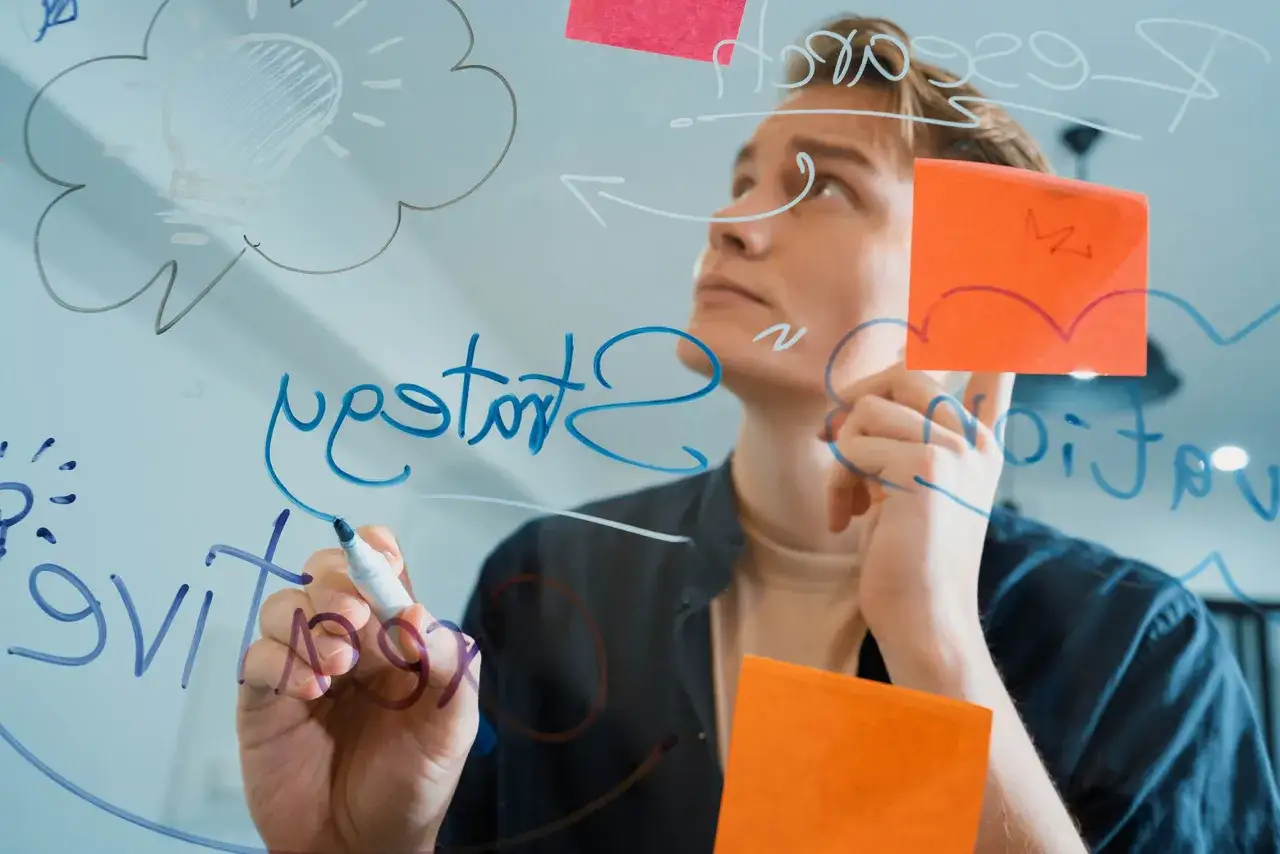 Młody mężczyzna pisze na szkle, tworząc schemat myśli i notując pomysły. To wizualizacja tego, jak uczyć się efektywnie.