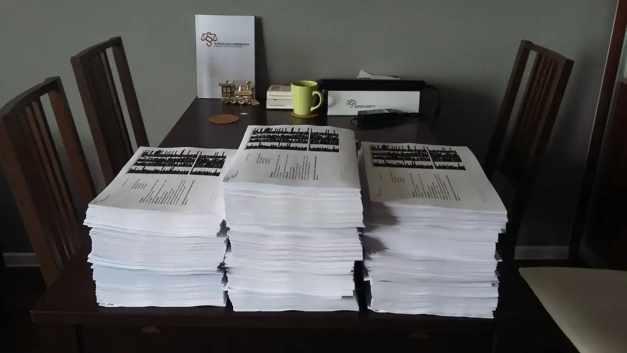 Stosy dokumentów na stole, obok nich dokument kancelarii adwokackiej. Gdy potrzebujesz pomocy, gdzie złożyć skargę na wspólnotę mieszkaniową, warto udać się do prawnika.