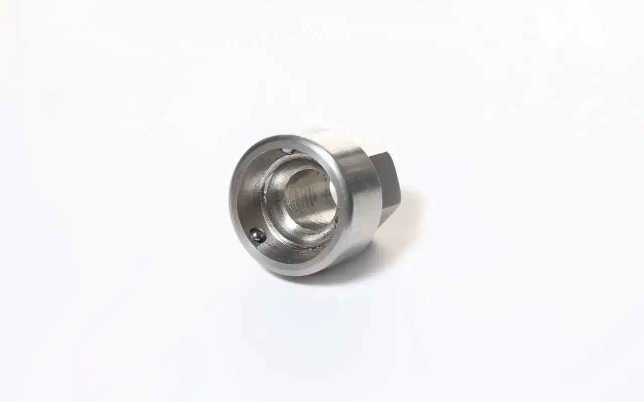 Metalowy, sześciokątny element z otworem w środku, z widoczną kulką wewnątrz. To uniwersalny klucz do śrub zabezpieczających.