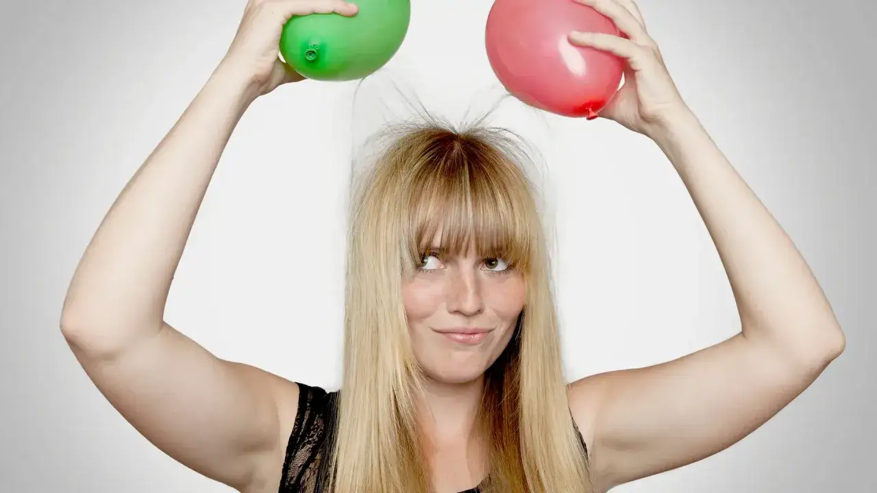 Dziewczyna z zielonym i różowym balonem nad głową, jej elektryzujące się włosy sterczą na wszystkie strony.