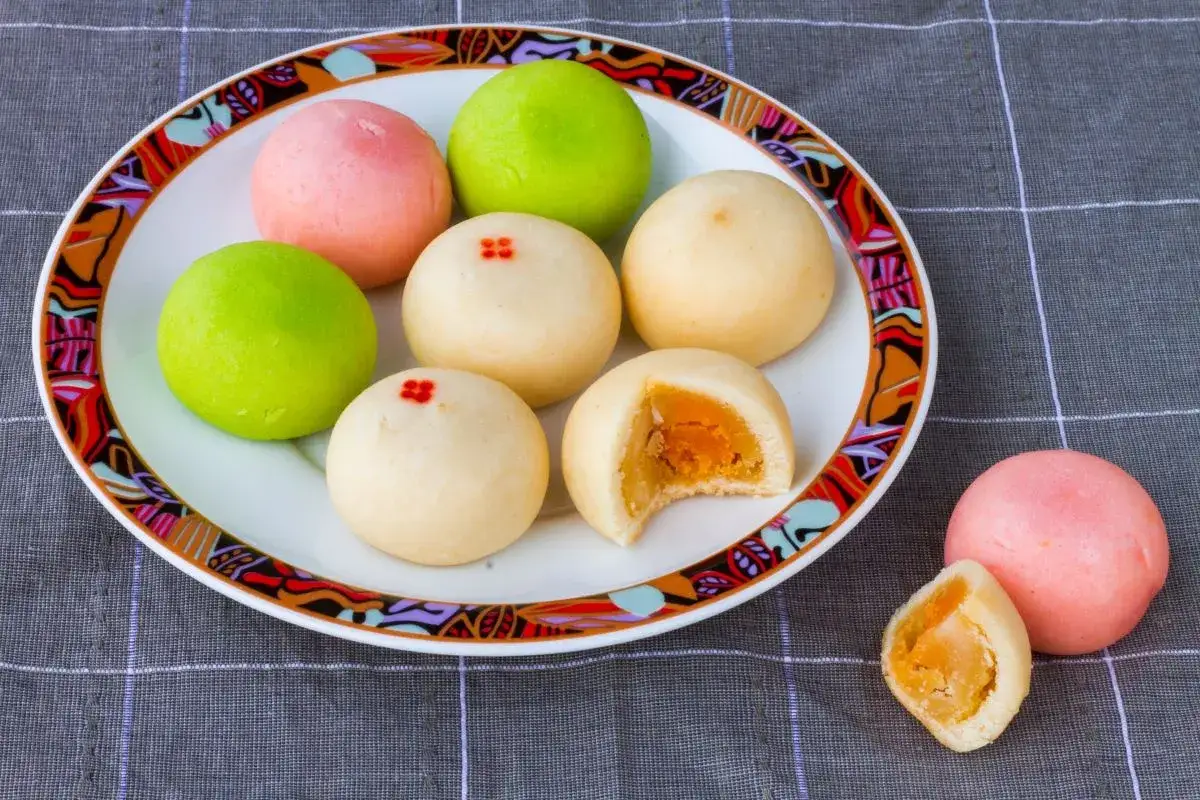 Kolorowe mochi z żółtym nadzieniem na talerzu z ozdobnym brzegiem.