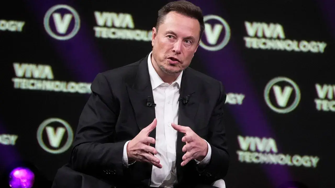 Elon Musk w garniturze, przemawiający na tle logo Viva Technology.