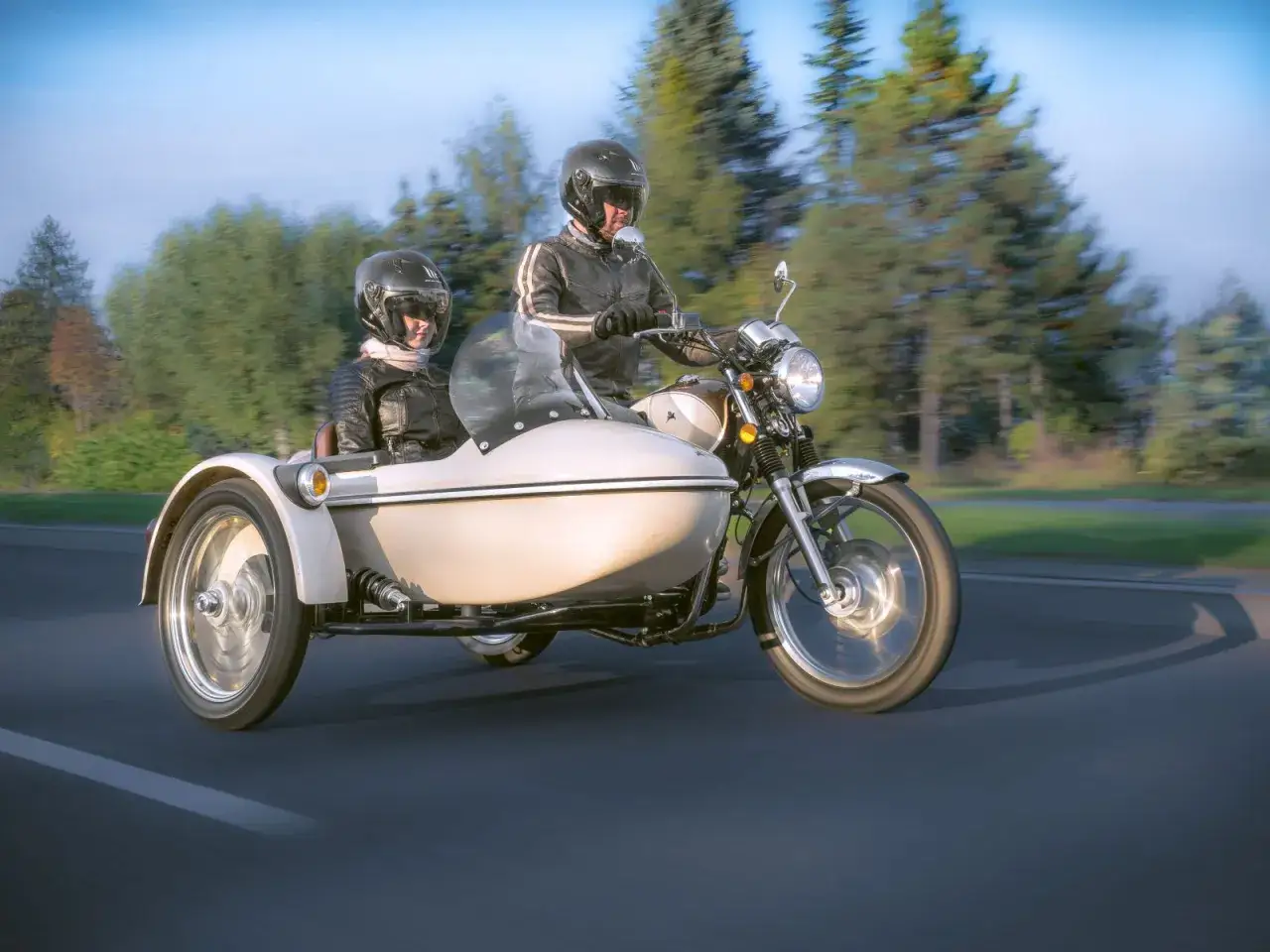 Para podróżuje motocyklem z koszem, ciesząc się jazdą po malowniczej drodze.