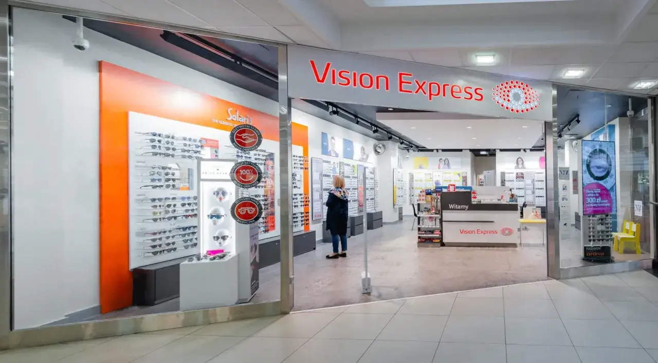 Sklep Vision Express z ekspozycją okularów i kobietą przeglądającą ofertę.