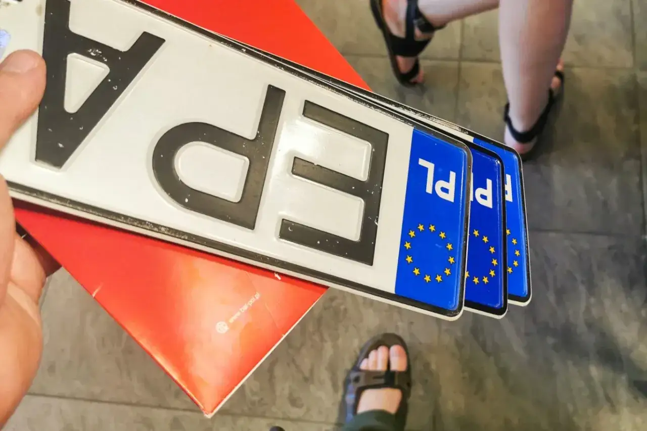 Kilka nowych tablic rejestracyjnych PL leży na czerwonym podkładzie.