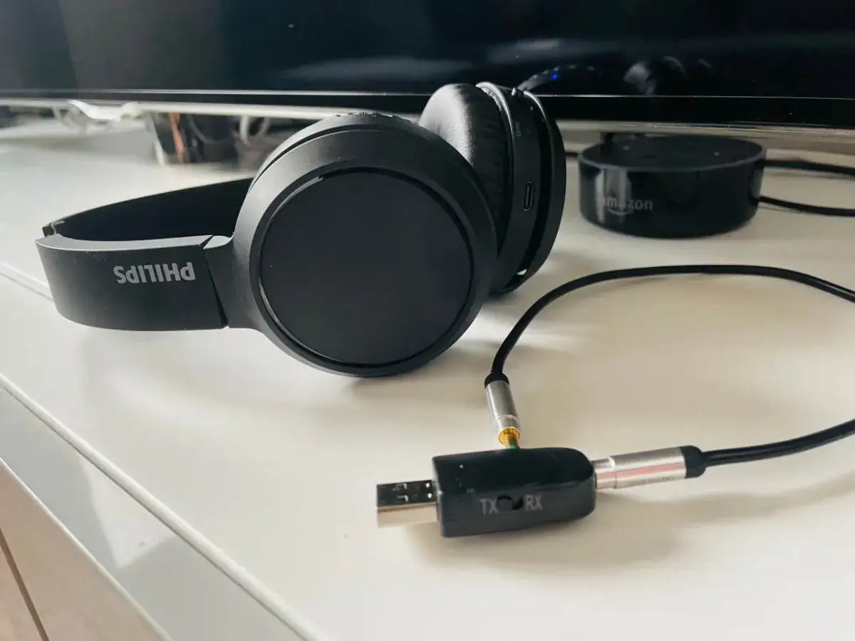 Czarne słuchawki Philips podłączone do adaptera Bluetooth TX/RX na białym blacie.