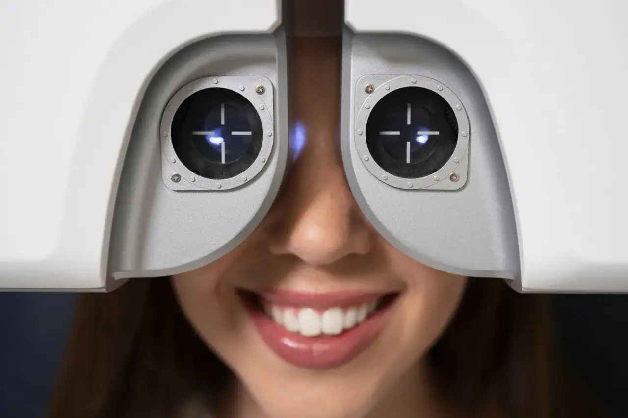 Uśmiechnięta kobieta podczas badania wzroku za pomocą urządzenia optometrycznego.