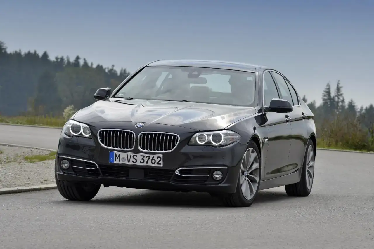 Ciemnoszary sedan BMW F10 na drodze, z widokiem na las. Idealne wymiary dla komfortowej podróży.