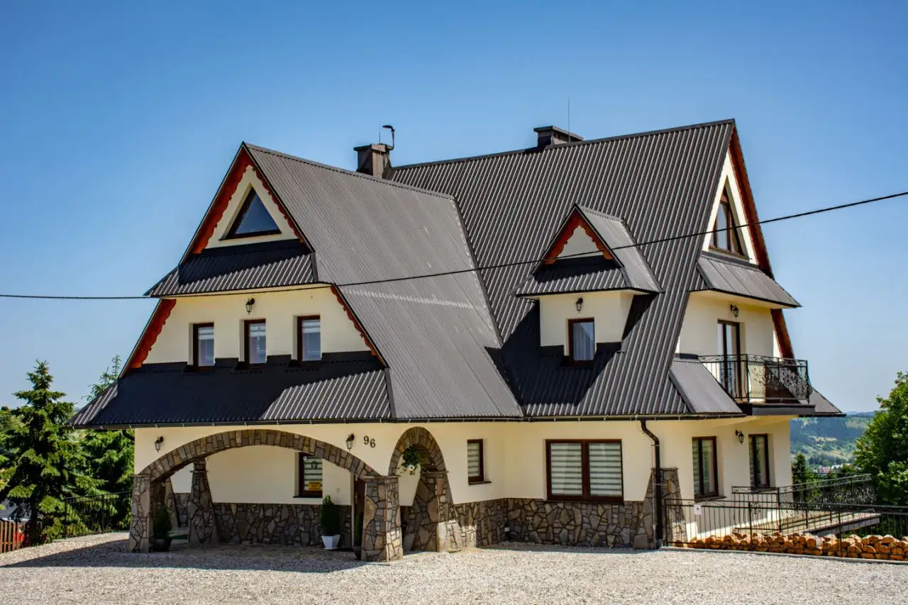 Willa pod Zielonym Wierchem w Zakopanem, z kamiennym łukiem i wielospadowym dachem, zaprasza na wypoczynek w górskim klimacie.