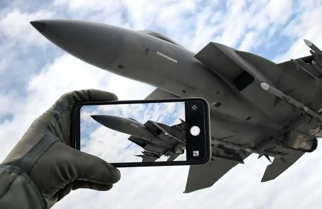 Ręka w rękawicy pilota trzyma smartfon, na którym widać myśliwiec. To jakby zapowiedź **Top Gun 3** – uchwycone w kadrze marzenie o przestworzach.