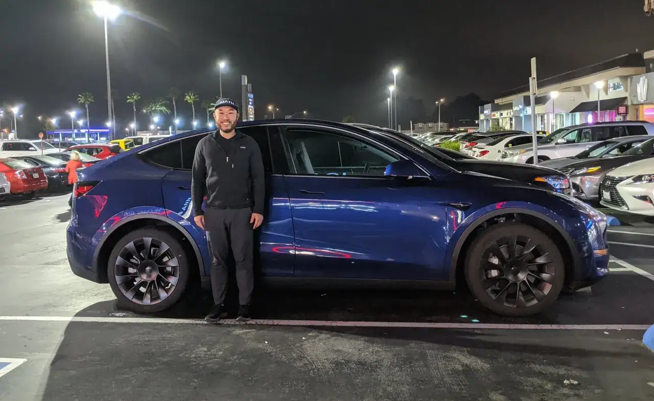Mężczyzna stoi obok swojego niebieskiego Tesli. Zastanawiasz się, ile waży Tesla? Ten model waży około 2 ton.