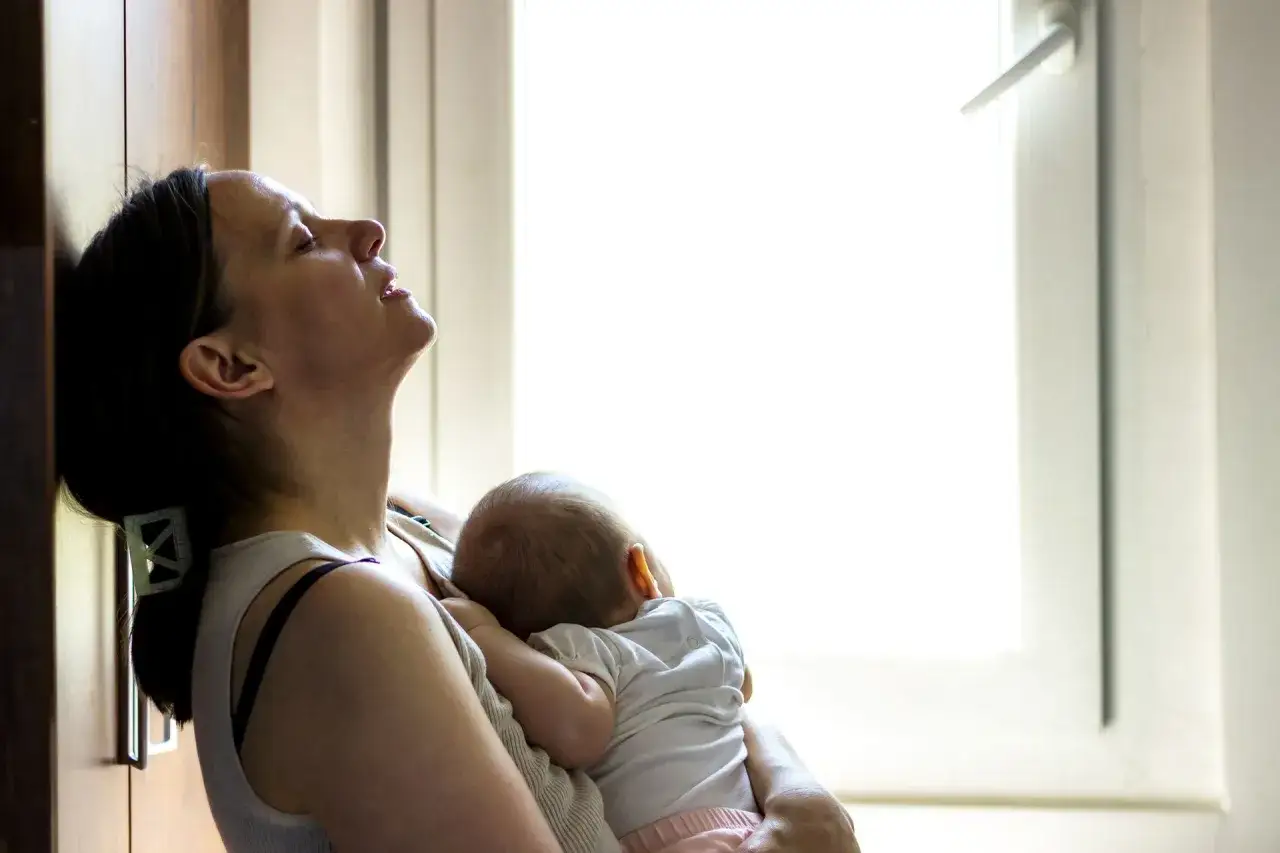 Zmęczona mama tuli śpiące dziecko. Czas po porodzie bywa trudny, ale miłość do malucha daje siłę.