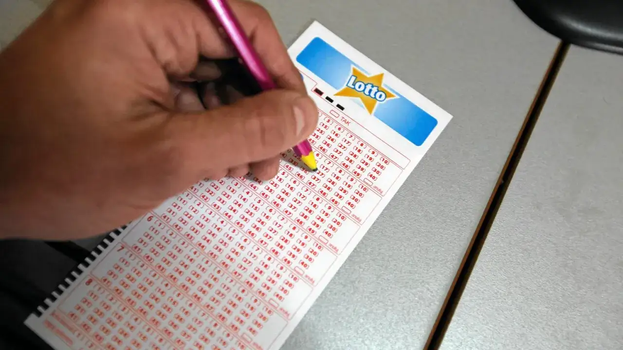 Ręka z ołówkiem zaznacza liczby na kuponie Lotto. Czy na Orlenie jest Lotto? Sprawdź, wypełniając swój kupon!