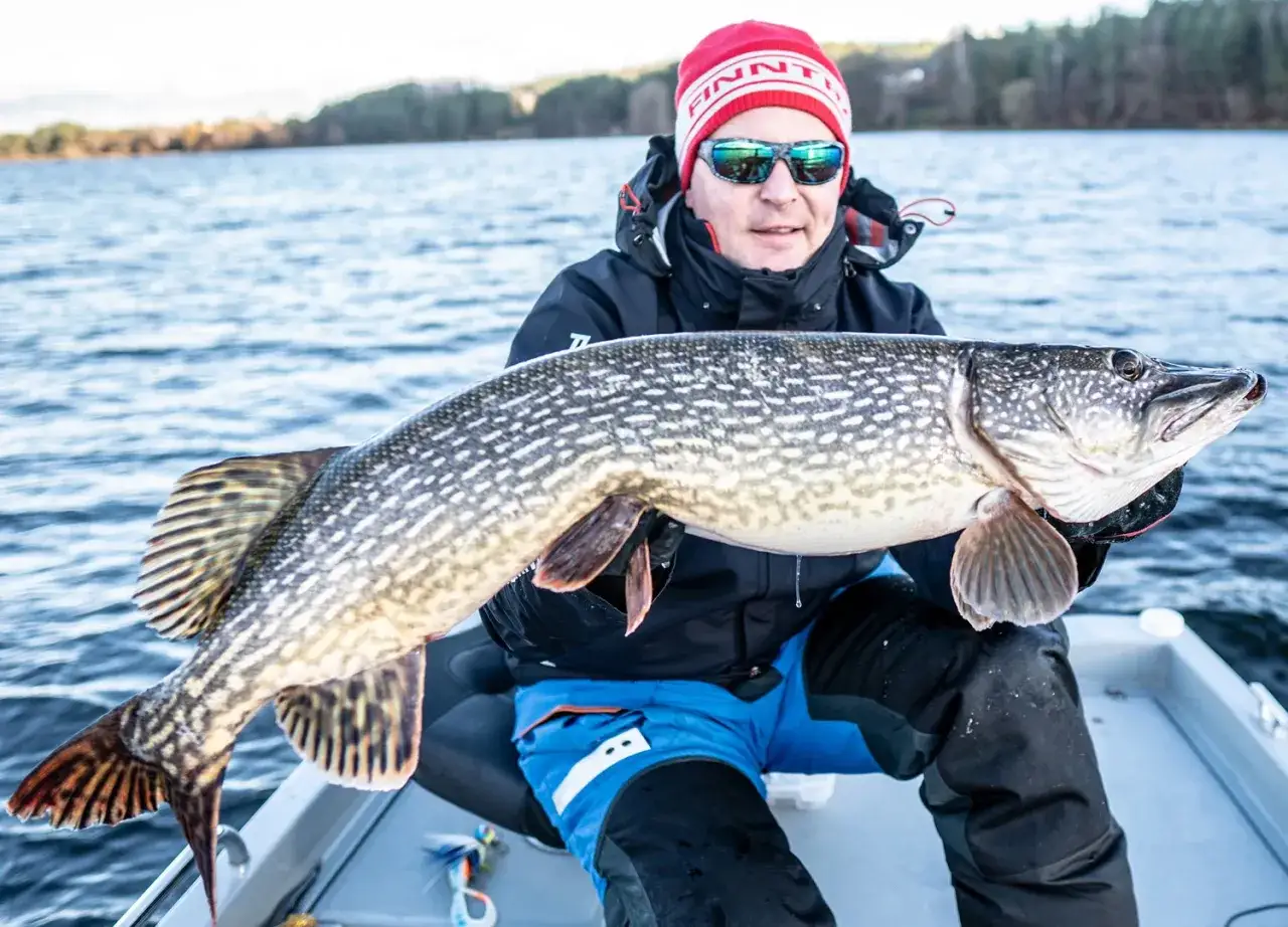 Szczęśliwy wędkarz z okazałym szczupakiem na tle jeziora. Udany połów na łowisku Kaszyce Milickie.