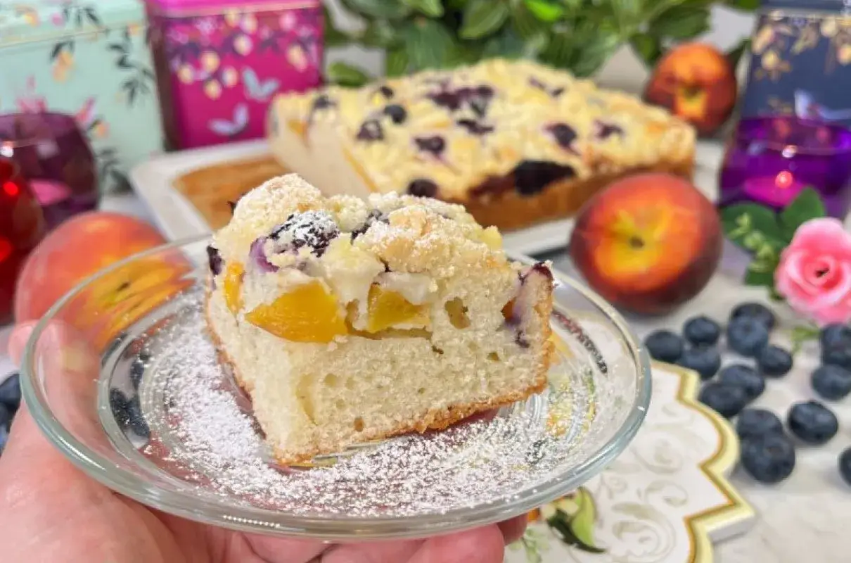 Pyszne ciasto widelcem mieszane z brzoskwiniami i borówkami, posypane cukrem pudrem. Idealne na deser.