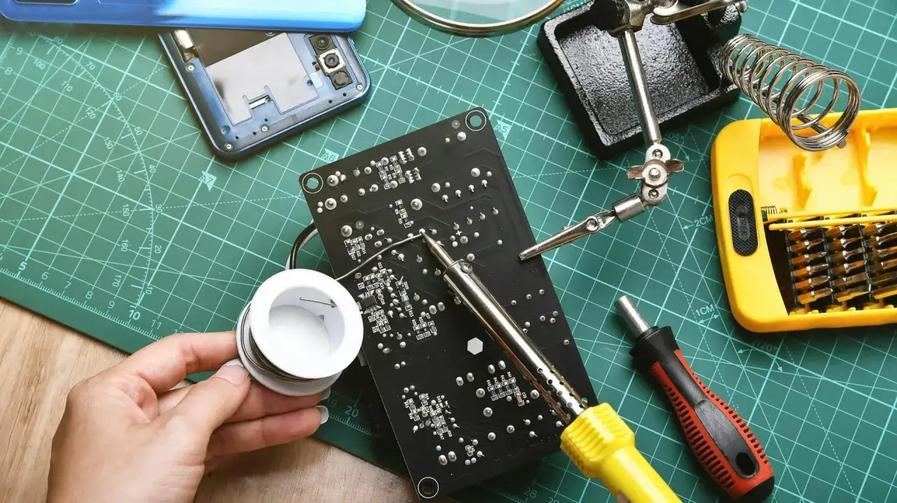 Ręka trzymająca cynę do lutowania, obok lutownica i płytka drukowana. Idealny zestaw, by dowiedzieć się, jaka lutownica do kabli będzie najlepsza.