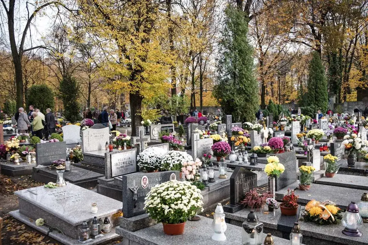 Jesień na cmentarzu komunalnym w Katowicach. Ludzie odwiedzają groby, składają kwiaty i zapalają znicze.